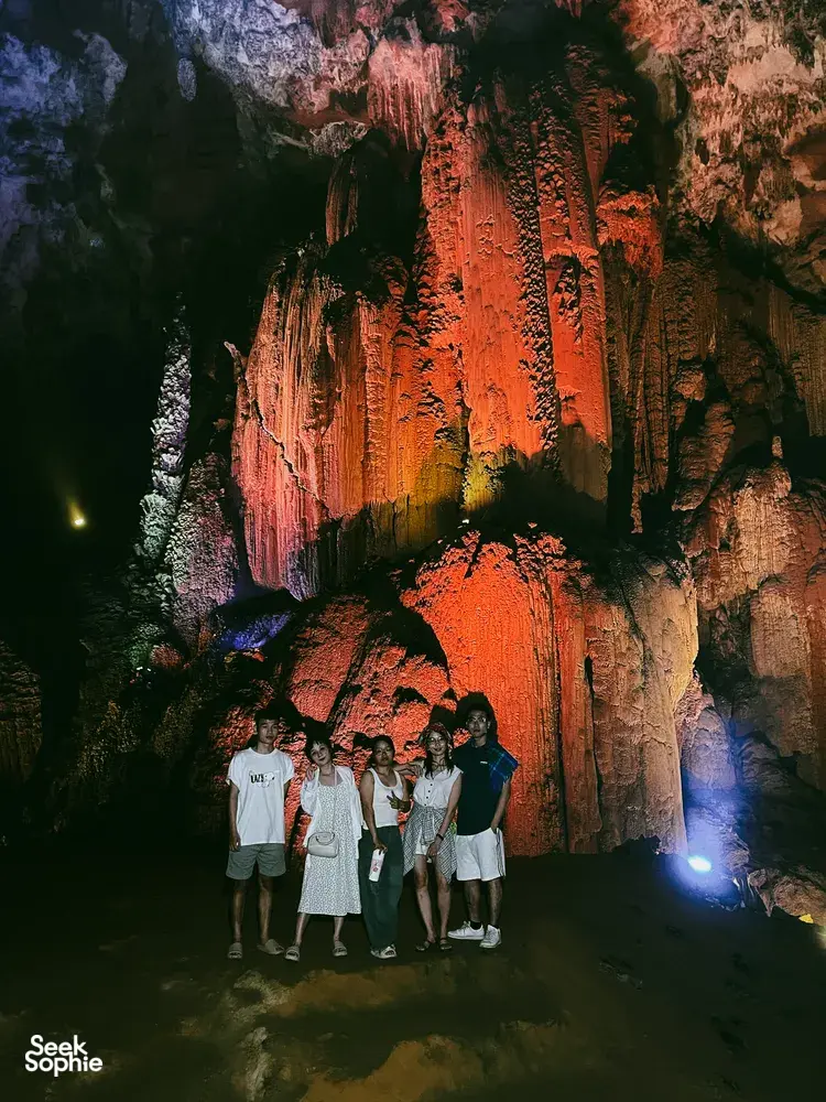 Group of travellers standing under dramatic cave lighting with a rocky ceiling during the Cao Bang motorbike adventure