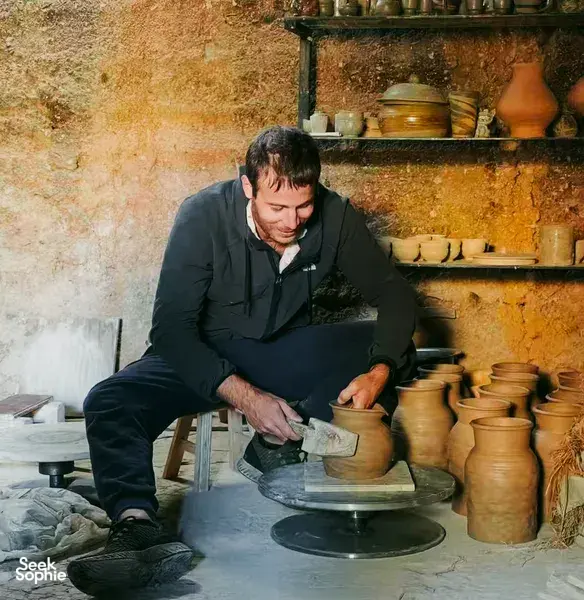 Potter working at a wheel in an ancient pottery village in Dali, with clay jars and tools arranged along the wall