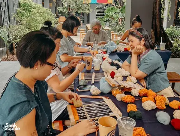 Small group weaving Thai textiles at Kalm Village in Chiang Mai, working together at hand-crafted looms with yarn skeins