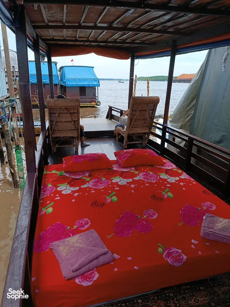 Outdoor boat deck with red bedding and two wicker chairs, set for relaxing between sightings on a 3D2N Sister Tour cruise, Tanjung Puting