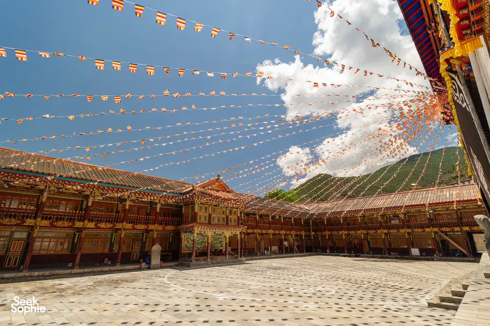 Courtyard walkway inside a Tibetan monastery in Shangri-La, lined with wooden rooms and strings of prayer flags fluttering above