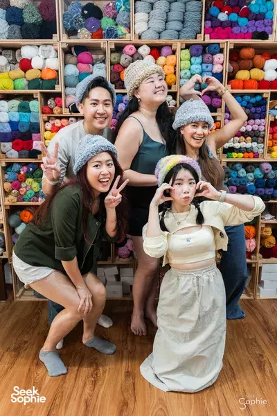 Tiny Rabbit Hole Singapore participants posing with grey plush hats beside colourful yarn shelves — workshops in Singapore