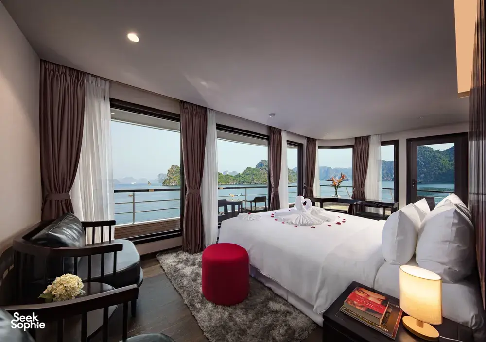 Oasis Bay Party Cruiser suite with a made-up double bed and large windows opening to the sea-facing deck, on the Halong Bay