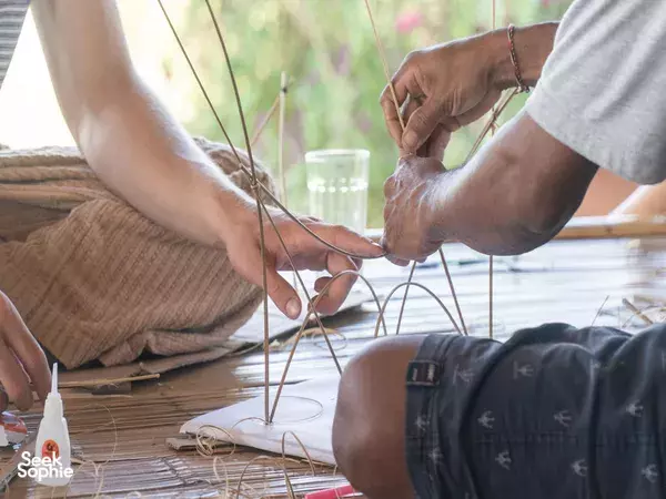 Close-up of hands tying bamboo rods with wire and twine during a Bali bamboo building design workshop