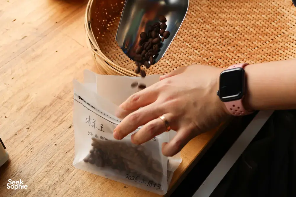 Hands packing freshly roasted coffee into labelled paper bags at Seeker Yunnan Coffee Estate in Lijiang