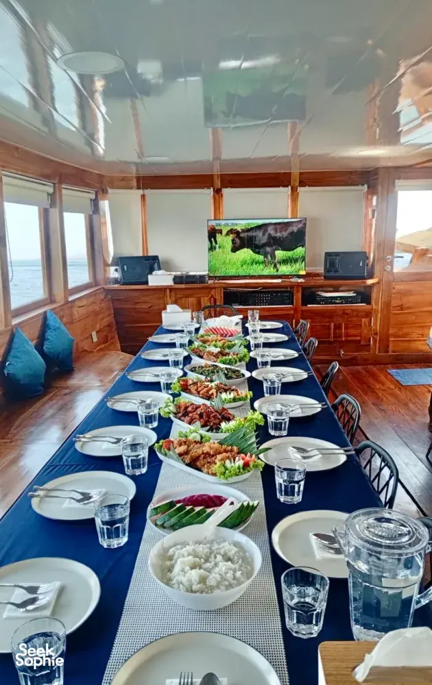 Set dining table aboard a wooden phinisi with shared plates, bowls and drinks during a 3D2N cruise to Komodo Island