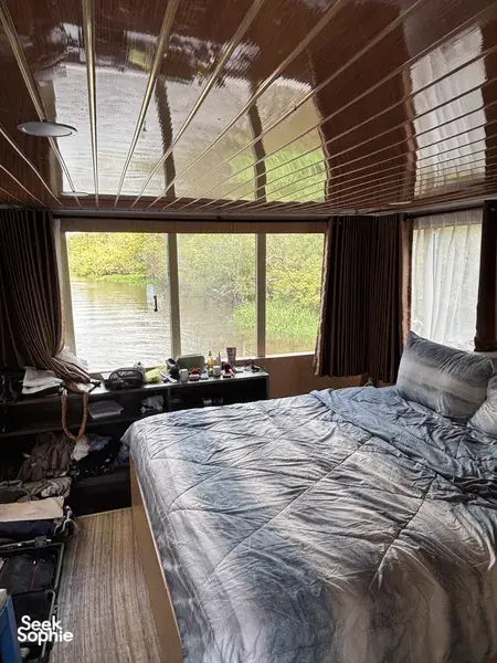 Air-conditioned houseboat cabin interior with a large bed and open window overlooking the river in Tanjung Puting