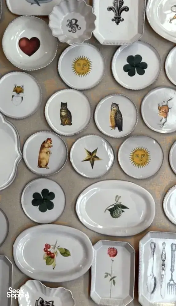 Assortment of small decorative ceramic plates with animal, flower and sun motifs arranged in rows on a display table
