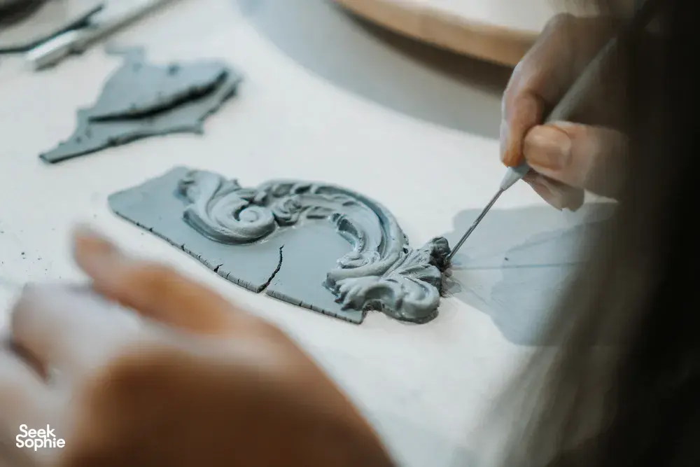Hands carving an antique-style ceramic plate ornament with a needle tool at Ina Atelier pottery workshops in Singapore