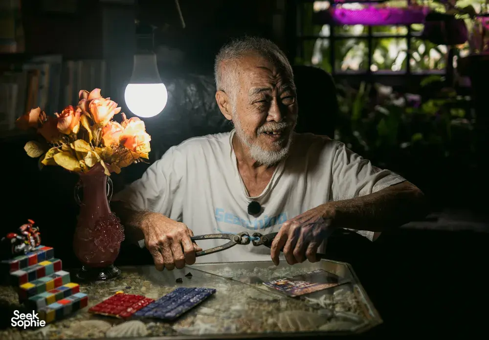 Lelaki meneliti kertas dan objek di atas meja dalam bilik bercahaya lembut, untuk kisah apartmen sewa Hidden Heritage dan permata tersembunyi Singapura