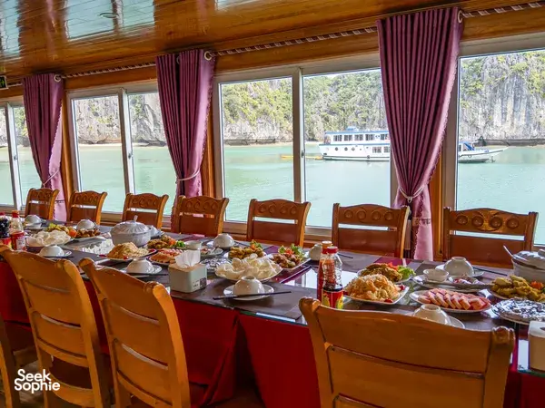 Table set with breakfast on board the Cat Ba Ventures 2D1N Lan Ha Bay cruise, with calm water and boats outside the windows