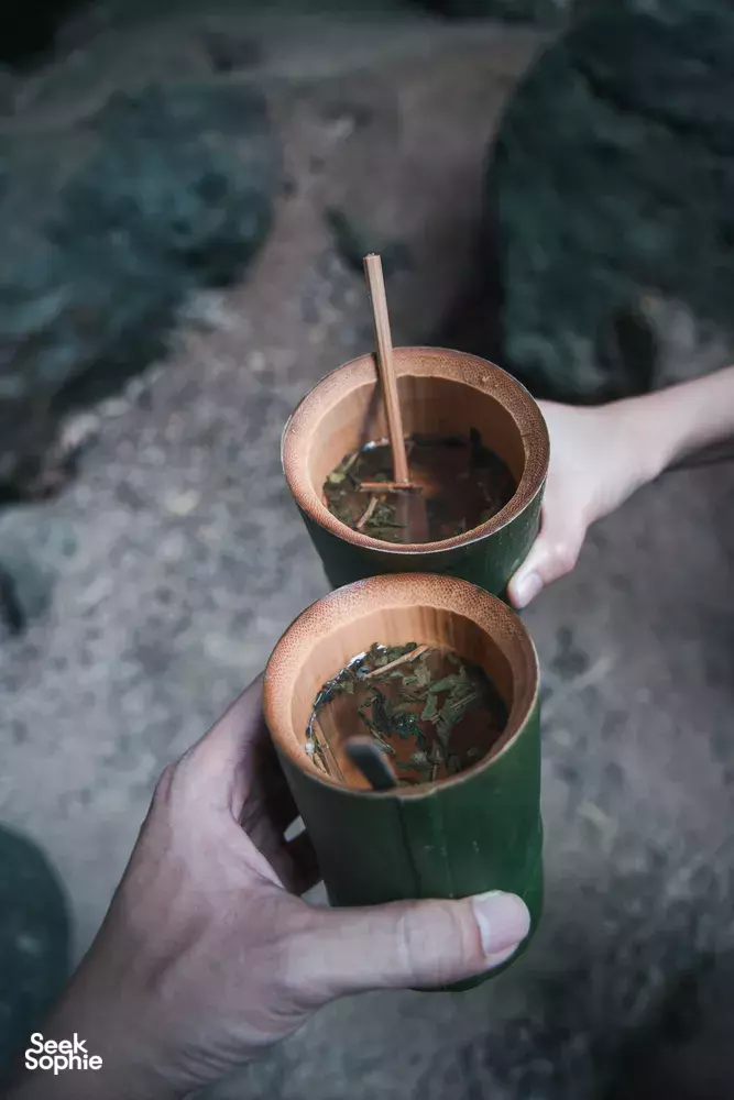 Bamboo cups of herbal drink clink in someone's hands during jungle dining at the eco-retreat, Khao Sok National Park