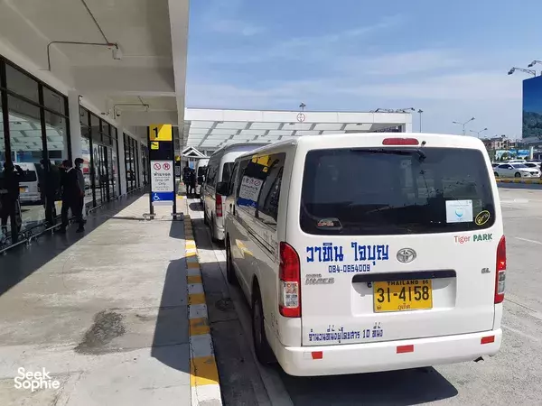 White shuttle minibus parked at a transport terminal in Phuket, Thailand, with people waiting on the platform