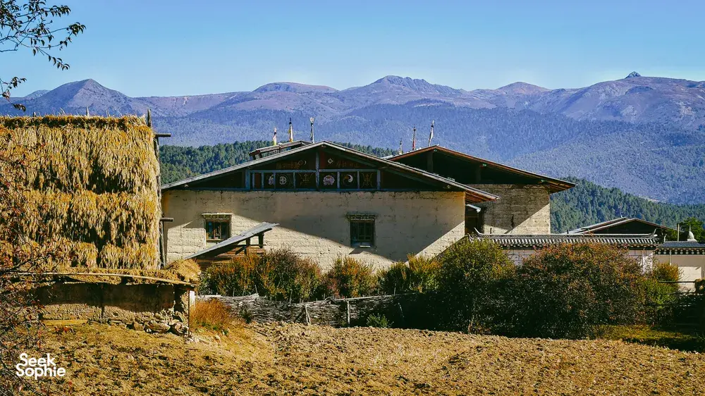 Tibetan lodge building at Ferme Liotard in Shangri-La, set on a hillside above farmland with distant mountain ridges