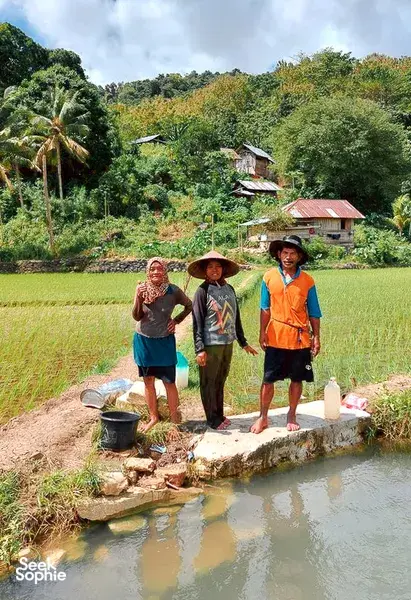 Travellers walking beside a village pond with rice fields during a hidden mangroves and village visit day trip, Labuan Bajo