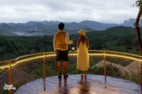 Lounge-deck at a luxe Khao Sok glamping stay, with two travellers by lantern light overlooking misty jungle mountains in Khao Sok National Park