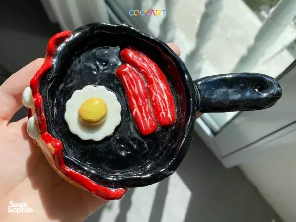 Hand holding a glossy black frying-pan-style ceramic mug with egg and red toppings at CocoArt SG in Singapore, workshops in Singapore