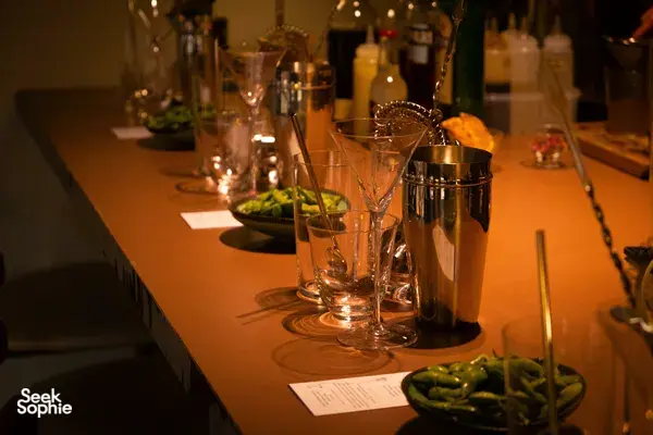 Glasses and cocktail serving tools on a warmly lit table in a Singapore cocktail bar, with candles and bottles glowing