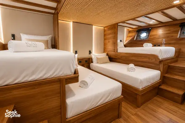 Travass Life shared cabin on a new phinisi with three neatly made single beds, wooden finishes and soft lighting for Komodo Island