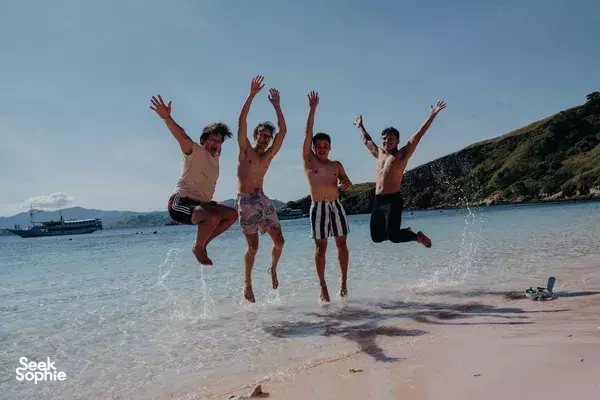 Group of travellers jumping from a sandy beach into shallow surf near cliffs while enjoying a rare 4D3N trip to Komodo Island