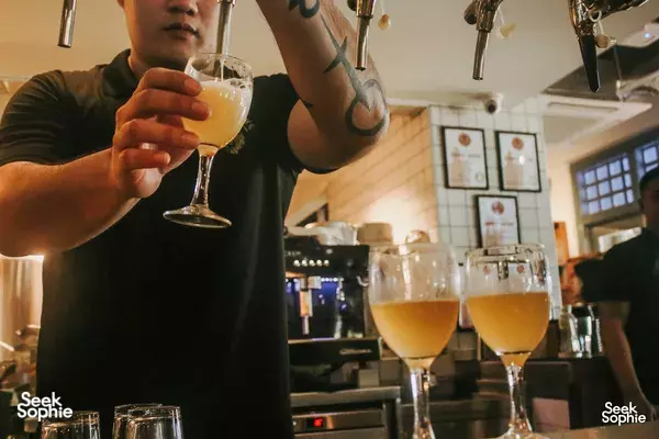 Taster holding a glass of pale beer at Lion Brewery Co brewpub in Singapore, with several beer glasses on the counter