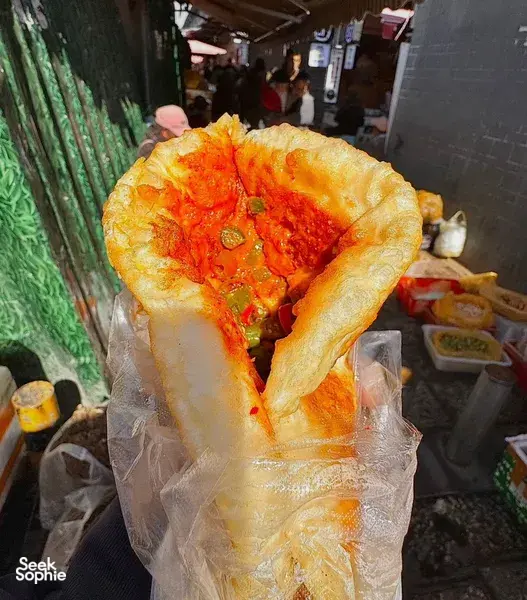 Folded, golden flatbread with bright red chilli filling wrapped in paper at a Lijiang street food stall