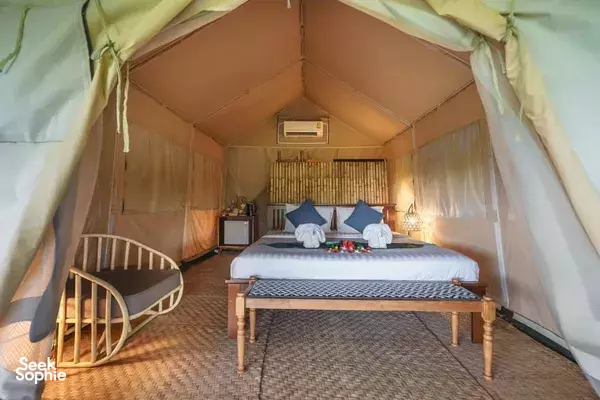 Luxury safari tent interior with a made bed, folded blankets and warm floor lighting under cream canvas walls in Khao Sok