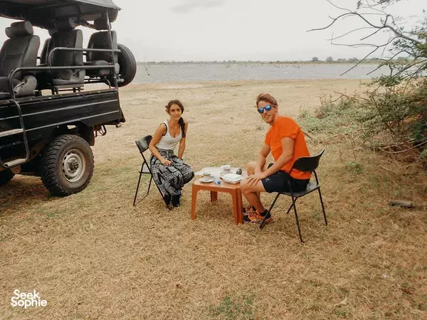 Travellers enjoying an open-air picnic by a safari jeep, seated at a small table in the grass near Udawalawe