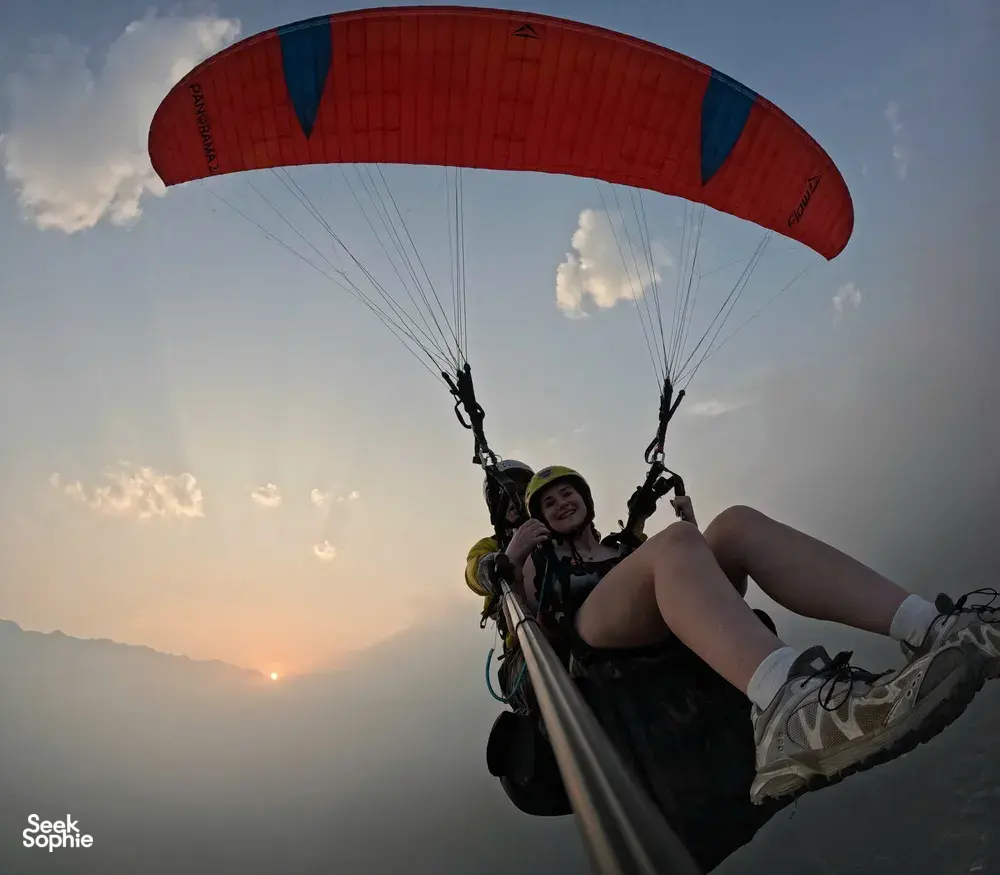 Silhouetted paragliding rider with a red canopy at golden hour, overlooking valley scenery from above the clouds in Sapa