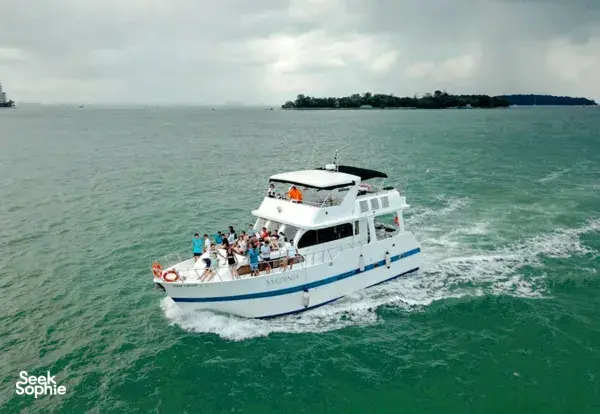 Large 57ft yacht with a team party crowd on deck, cruising from Singapore towards Lazarus Island at sea