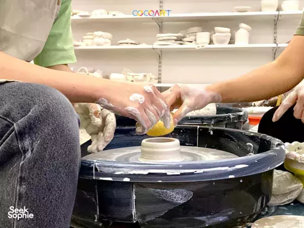 Hands smoothing wet clay on a pottery wheel during a pottery session in Singapore, workshops in Singapore