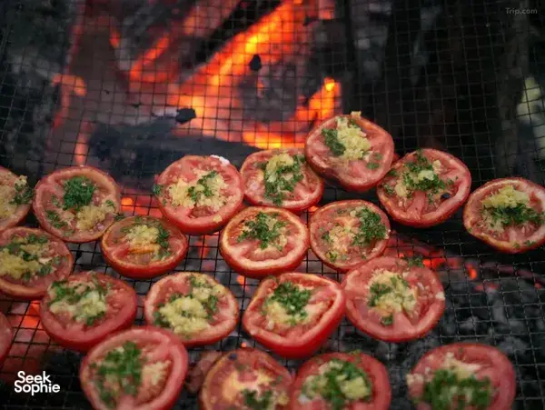 Grilled chicken and tomatoes with chopped herbs cooking on an outdoor fire rack at a mountain valley camp in Shangri-La