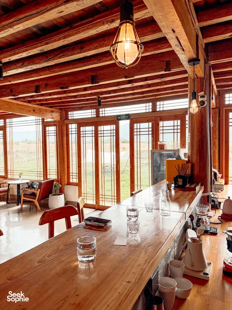 Sunlit interior of a family-run coffee workshop in Lijiang, with a long wooden tasting table, hanging lamps and countryside views