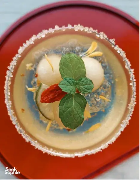 Herbal infusion in a red bowl for TCM mocktails, garnished with mint leaves and sliced roots during workshops in Singapore