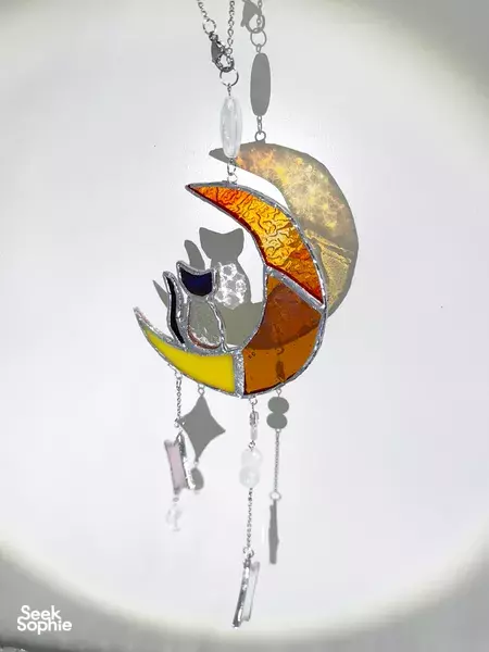 Crescent-moon and cat stained-glass suncatcher hanging on a silver chain with beads, displayed on a light wall at workshops in Singapore