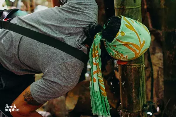 Jungle campsite in Kota Kinabalu: camper adjusting a green patterned headscarf and gear beside a wooden post