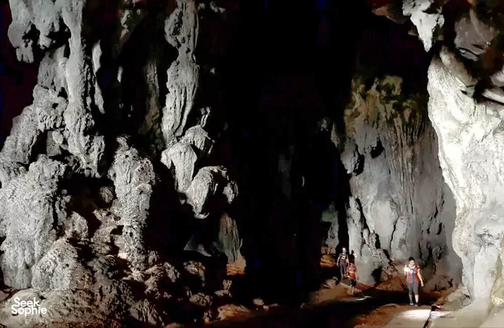 Rocky cave entrance with travellers walking along a dim chamber near Kuching on a gold-mine and jungle adventure