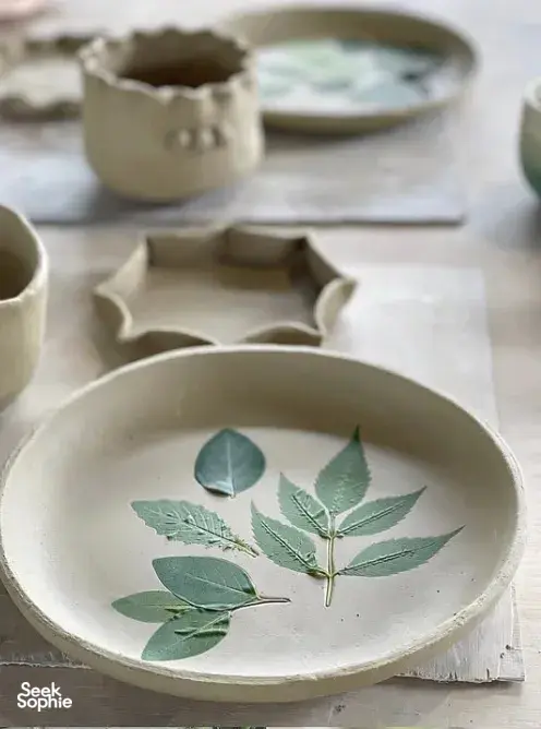 Hand-painted ceramic bowl with a botanical leaf design at Ilham Ceramic Studio in Langkawi, with other pieces in soft focus.