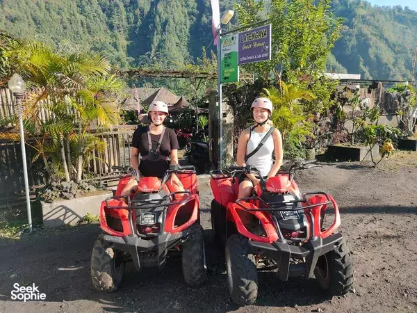 Two helmeted riders pose on red ATVs with mountain valleys behind during a Bali ride, at Mt Batur