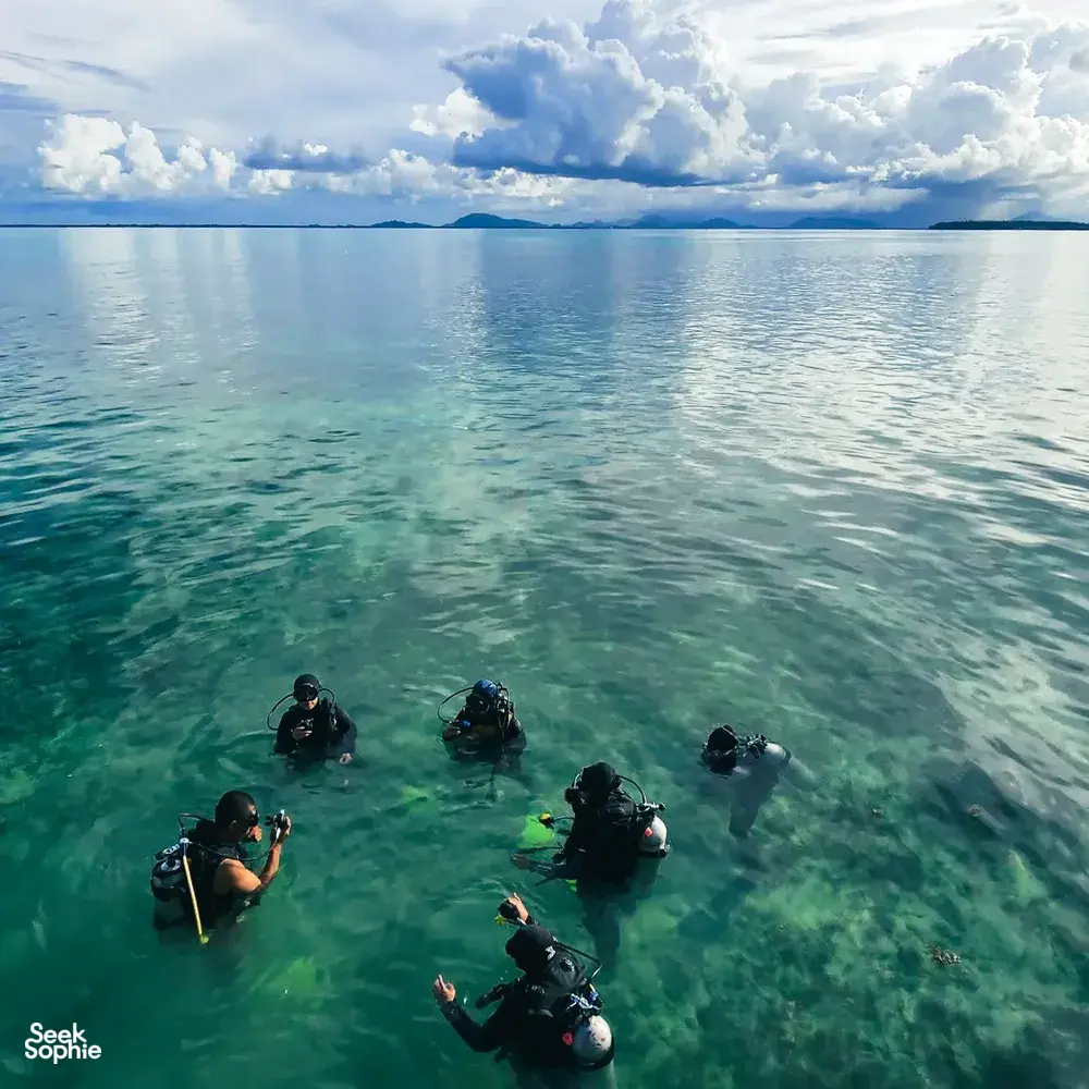 Scuba divers equipped with fins and tanks floating over clear shallow reef water off Semporna for a 2D1N dive & stay