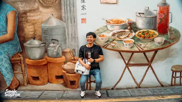 Tour participant holding a booklet and standing in front of a painted hawker stall with pots and noodle dishes in Singapore