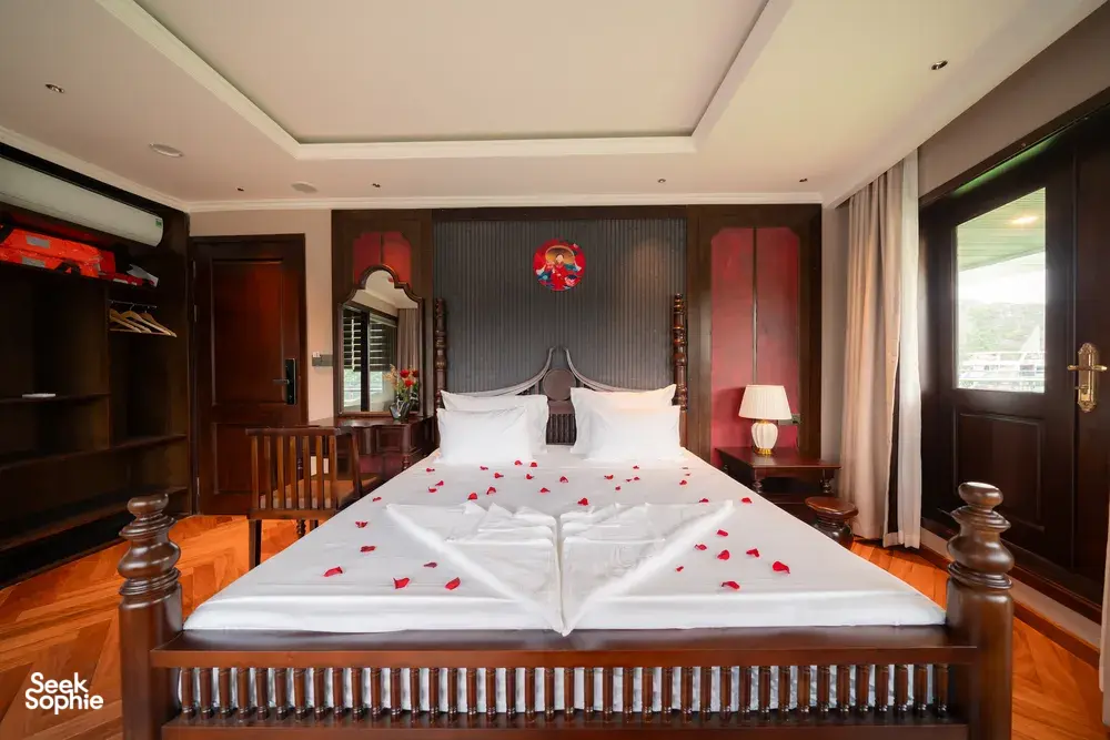 Luxe cruise bedroom with king bed, rose‑petal towel swan decoration, built-in wardrobe and curtains, Cat Ba 2D1N