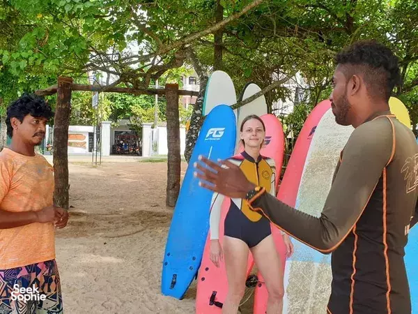 Surfers with colourful boards stand under trees at a Weligama surf base before paddling out for a group session