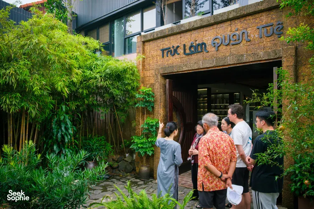 Group entering a Hanoi courtyard workshop through an arched doorway bordered by bamboo plants and lush greenery