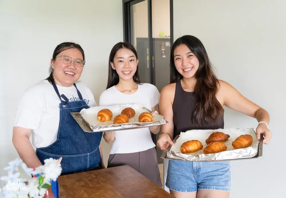 Three women laughing and posing with trays of shio pan buns made with flavoured butter during hands-on workshops in Singapore