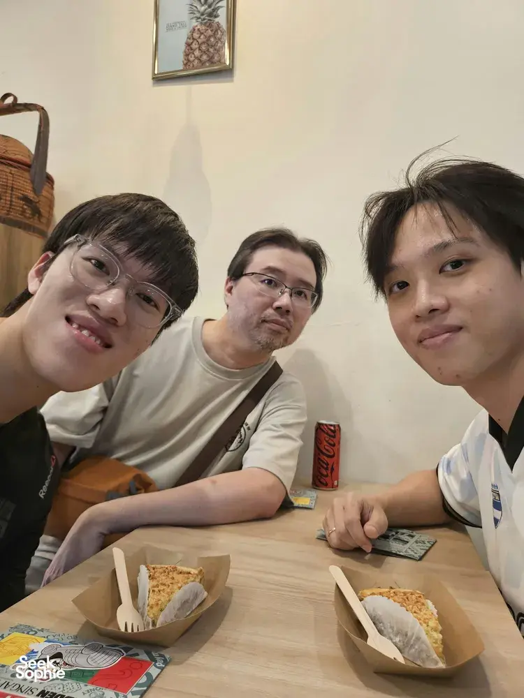 Friends seated at a wooden table with takeaway sandwiches during an indoor Monopoly-style game briefing in Singapore hidden gems.