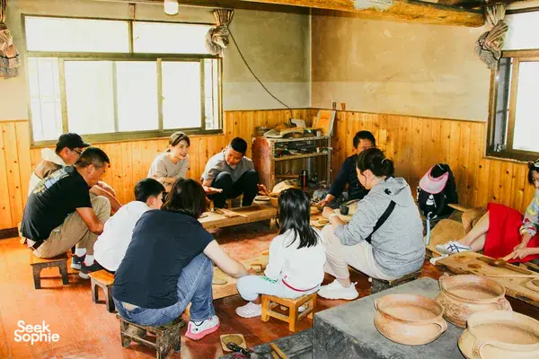Pottery workshop in Shangri-La with a small group shaping clay at wooden tables, inside a warm community room