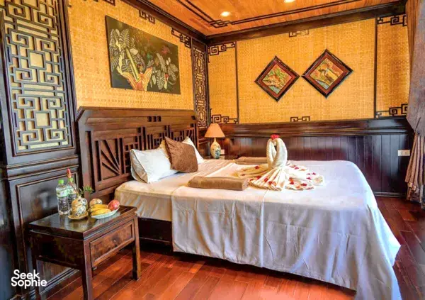 Cat Ba Ocean Cruises wooden cabin with a double bed, patterned wall art and bedside drinks, cosy retreat in Halong Bay