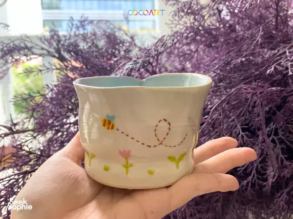 Hands holding a small pastel-painted ceramic bowl outdoors by purple foliage in Singapore, workshops in Singapore