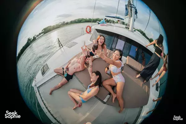 Friends lounging with drinks on the upper deck of a luxury catamaran cruising on smooth waters off Singapore